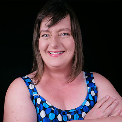 Portrait of Ginny Evans-Pollard smiling with her arms crossed against a black background.